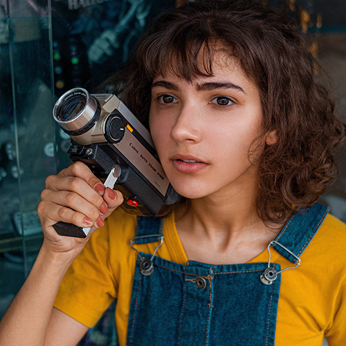 A photo of a young girl in overalls holding a video camera.