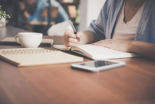 A person sitting on a desk writing in a notebook.