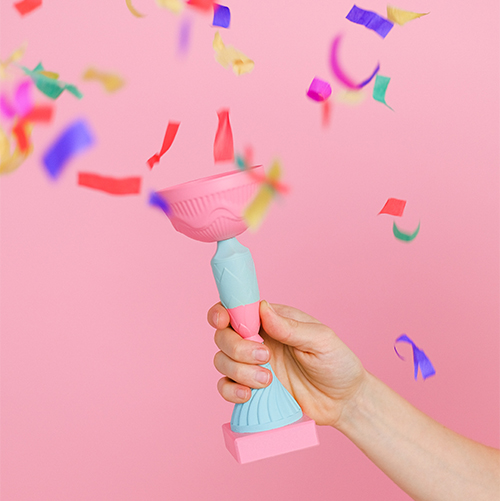 winner, hand holding a trophy on a pink background with confetti flying around