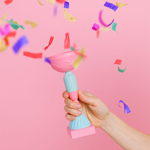 winners winner, hand holding a trophy on a pink background with confetti flying around